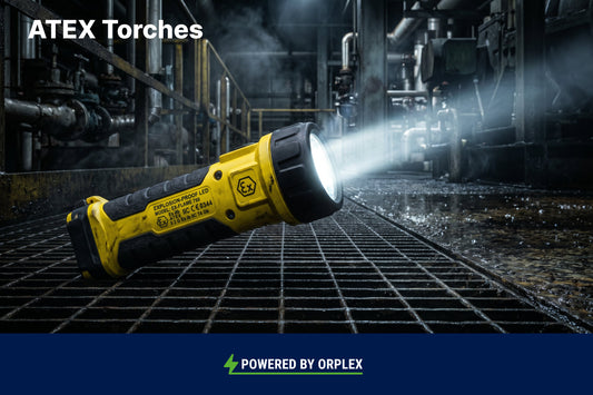 Yellow industrial ATEX torch resting on a metal grate floor, casting a bright beam of light into a dark factory setting.